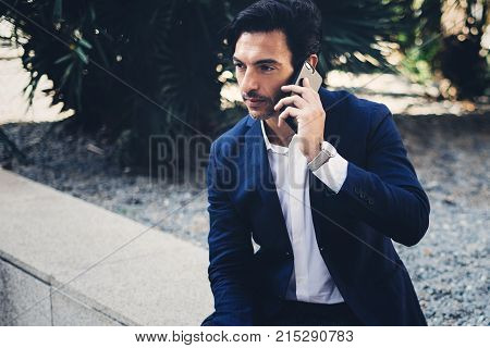 Elegant young businessman working outside with mobile laptop pro. Handsome man using modern smartphone for call.Blurred background.Horizontal.Cropped