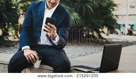 Attractive smiling businessman making video conversation with partners by mobile phone.Man using contemporary smartphone sitting outside.Blurred background. Horizontal. Cropped
