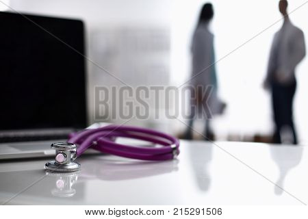 Laptop and medical stethoscope on the desk , doctors standing in the background.