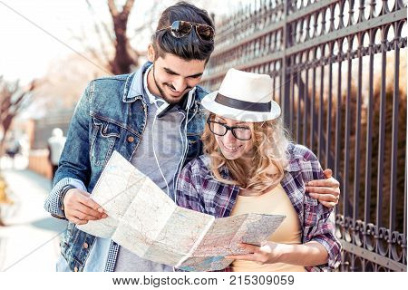 Loving couple with the help of a map is looking for an address on the strreet.