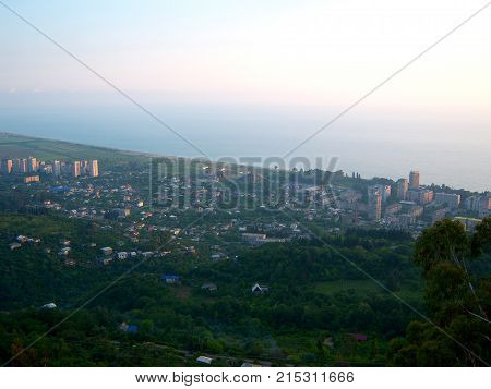 Panorama of the city of Gagry. View from a height of one kilometer. Visible houses streets roads buildings of the city and adjacent fields. In the background is the Black Sea coast. Photo taken at sunset. A light haze covers the sea it gives an impression
