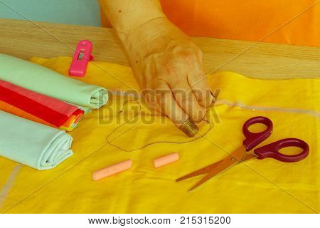 Woman hands sewing yellow dress from textile. needlework and hand quilting - tailor hands sew yellow with the use of needles