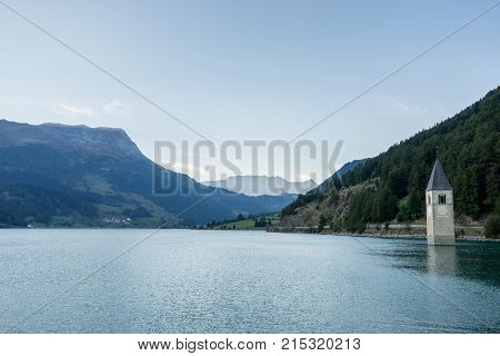 Church under water drowned village mountains landscape and peaks in background. Reschensee Lake Reschen Lago di Resia. Italy Europe Südtirol South Tyrol Upper Adige Alto Adige