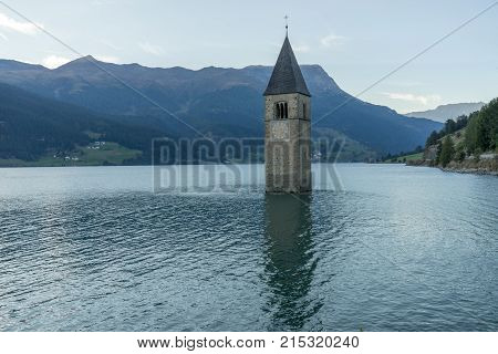 Church under water drowned village mountains landscape and peaks in background. Reschensee Lake Reschen Lago di Resia. Italy Europe Südtirol South Tyrol Upper Adige Alto Adige