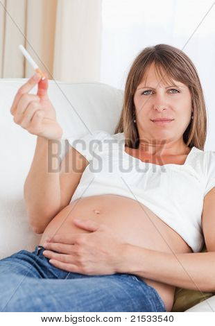 Wunderschöne schwangere Frau hält eine Zigarette beim liegen auf dem Sofa