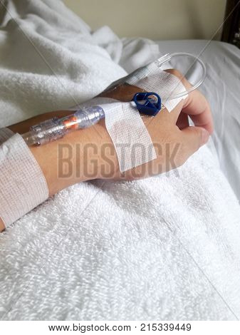 Patient hand with the tube of normal saline infusion on white cloth background