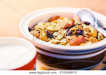 closed up of multi-grain cereal with dried fruits and nuts in an asian style bowl with cup of milk on wooden table in warm morning light room for text and copy space good for healthy diet lifestyle concept