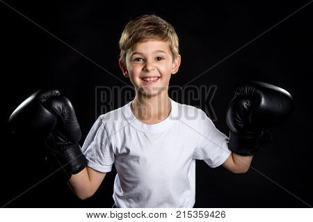 Extremely happy little boxer fighter portrait in black boxing gloves with hands up. The little winner.