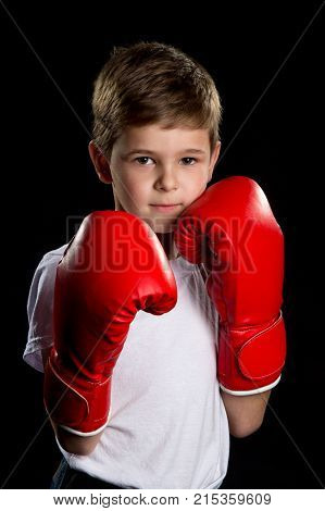 An angry, confident boxer with red gloves. Self defending position, boy portrait on the black background.
