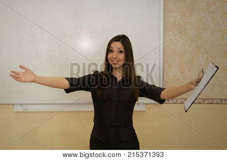 Cheerful teacher woman extends her hands forward and greets the students on school board background with copy space. Education concept.
