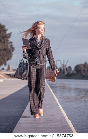 Vertical orange tonted shot of a beautiful blond woman walking with paper bags bag and tablet along the promenade