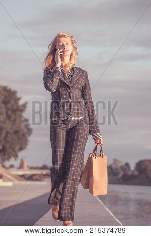 Vertical orange tonted shot of a beautiful blond woman walking along on the promenade with paper bags and talking on the phone
