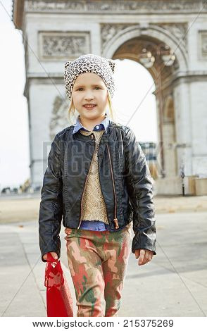 Stylish autumn in Paris. Portrait of modern girl with red present bag near Arc de Triomphe in Paris France going forward