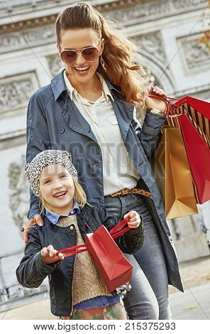 Stylish autumn in Paris. smiling young mother and child with shopping bags near Arc de Triomphe in Paris France having fun time