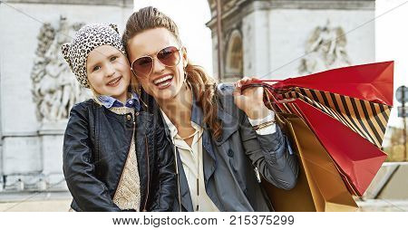 Stylish autumn in Paris. Portrait of smiling elegant mother and child with shopping bags near Arc de Triomphe in Paris France