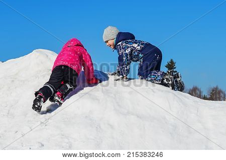 Winter fun children. A boy and a girl climb up of snow hill