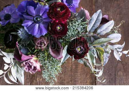 floral design, wedding decor, love concept. top view of adorable bouquet of different flowers, there are delicate pink roses, lilac anemones and dark maroon persian buttercups