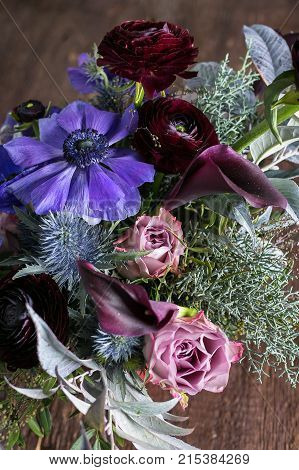 nature, wedding, present concept. close up of bunch composed of various flowers, simple lilac anemons, richy pink roses, maroon puffy buttercups and few thistles