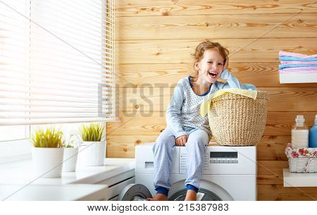 happy little funny housewife baby girl in laundry with washing machine