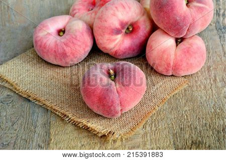 Saturn peach or Dough nut peaches on wooden background and sack cloth