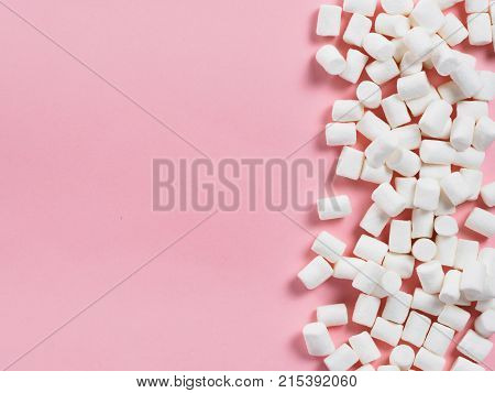 Marshmallows on pink background with copyspace. Flat lay or top view. Background or texture of colorful mini marshmallows. Winter food background concept.