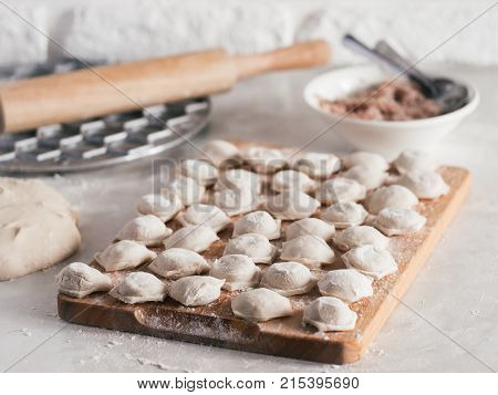 Uncooked russian pelmeni on cutting board and ingredients for homemade pelmeni on white table. Process of making pelmeni, ravioli or dumplings with meat. Copy space