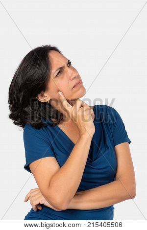 A woman thinkingwith one finger touching her face she is wearing a blue blouse