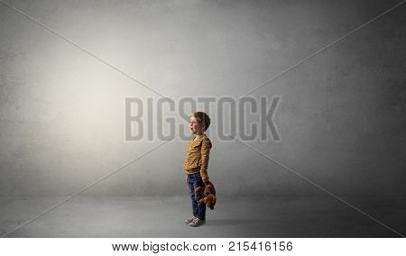 Little waggish kid staying alone in a big empty room with his plush