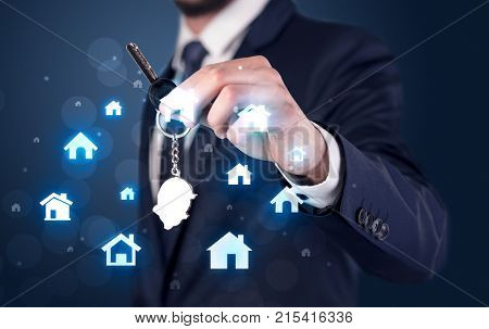 Businessman in suit holding keys with house graphics around and dark background