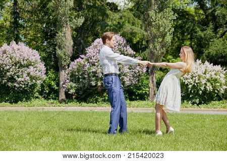 Young bearded man and woman poussette at green grassy lawn in park