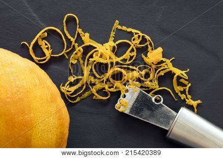 Orange zest and zester, top view, on dark slate.  With whole fruit.