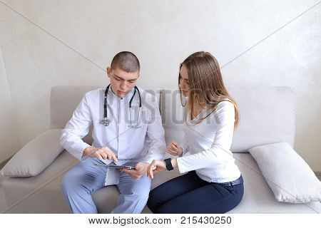 Female girl with iWatch on hand finds out from male doctor with gadget in hand how to use functions of modern electronic clocks to adjust proper sleep regime and feel good, therapist with stethoscope gives useful conclusions and writes pen to medical char