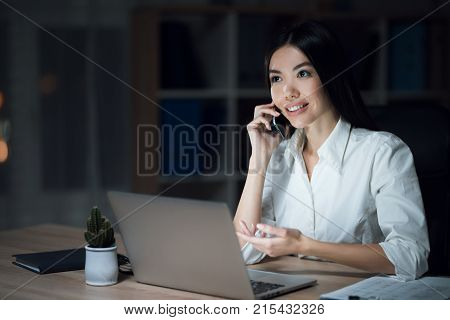 The girl is working late in the dark office with a laptop. Young beautiful businesswoman girl in office. Women talking on the phone in a dark office.