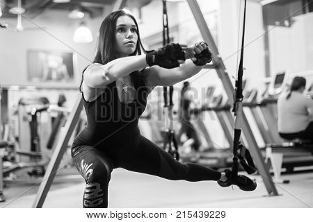 Athletic woman workout out squats weighted lunges exercise for butt legs with suspension straps in fitness club or gym