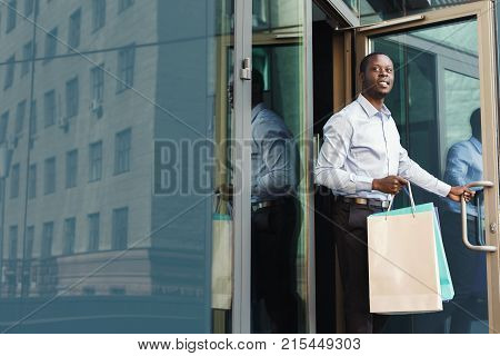 Happy black man with shopping bags walking out of modern boutique. Successful business and shopping concept