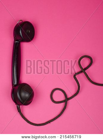 Vintage phone receiver with a cord on a bright pink background (minimal concept top view) with copy space for your text