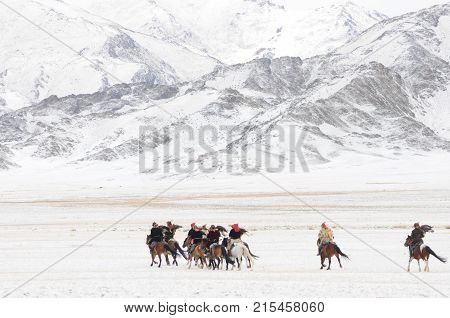 Mongolian men riding on horses in the opening of the golden eagle festival in  mongolia in the white snow mountains winter