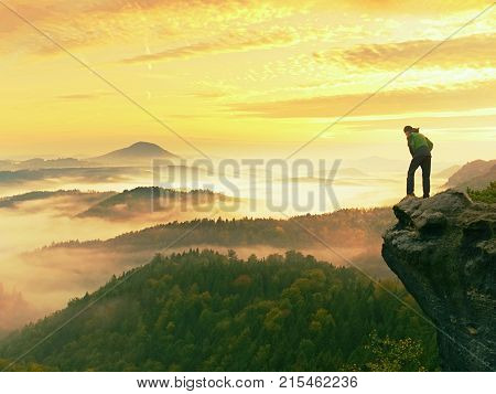 Man Stay On Rocky Peak Within Daybreak And Watch Over Misty Landscape.