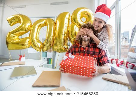 Happy guy holding giftbox while his gilfriend keeping her hands on his eyes