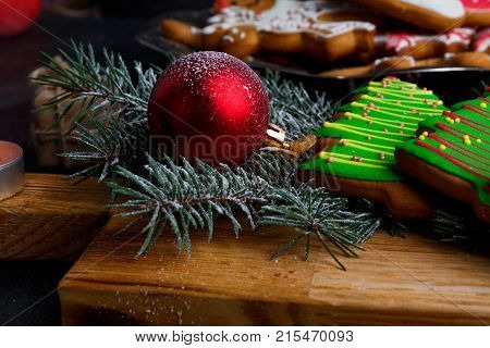 Close-up on a wooden board is a green Christmas tree-shaped biscuit, a red toy ball, a fir branch, a New Year's concept, a new year, Christmas.