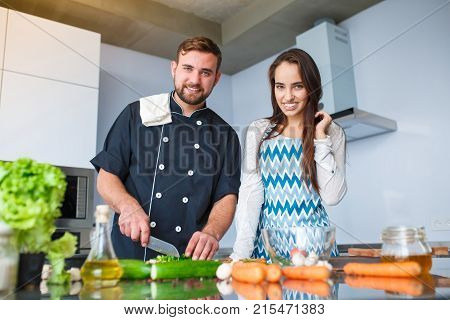 Young couple in the kitchen preparing food for dinner, watching the camera. Concept of cooking, family.