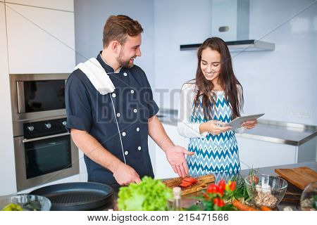 Young couple in the kitchen preparing food for dinner, watching the recipe on the tablet. Concept of cooking, family.