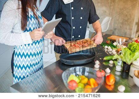 Young couple in the kitchen preparing food for dinner, watching the recipe on the tablet. Concept of cooking, family.