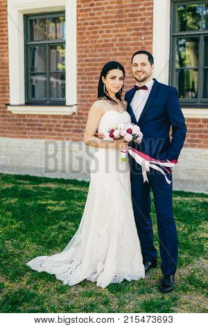 Vertical Portrait Of Happy Bride And Bridegroom Stand Next To Each Other, Wait For Guests, Celebrate