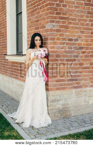 Thoughtful Brunette Female Bride In Beautiful Wedding Dress, Keeps Bouquete In Hands, Worries Before
