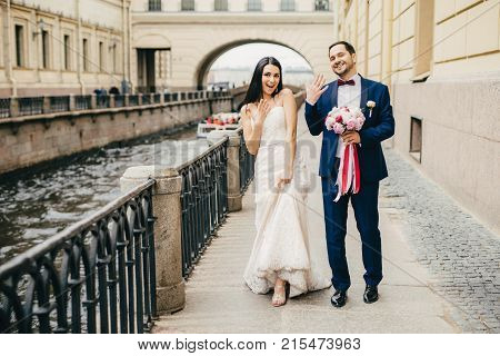 Excited Married Couple Show Rings On Fingers, Walk On Bridge, Poses At Camera To Make Unforgettable