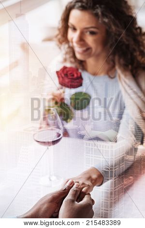 Unpredictable. Young delighted girl with curly hair and red rose looking at her man while holding his hand