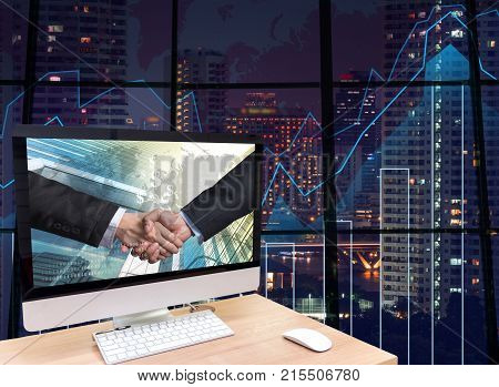the computer on the wood table with Hand shake between businessman at the screen on the trading graph over the blurred photo of cityscape background Elements of this image furnished, 