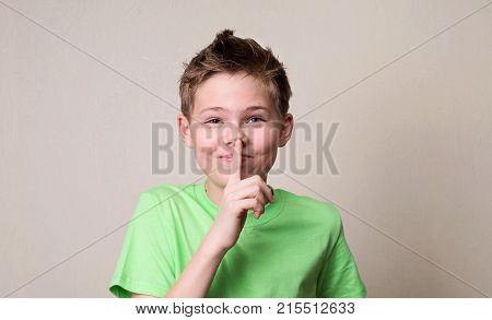 Laughing boy doing a silence gesture. Kid putting finger up to lips and ask silence.
