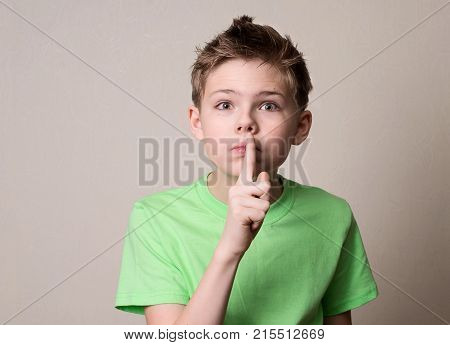 Scared boy doing a silence gesture. Kid putting finger up to lips and ask silence.